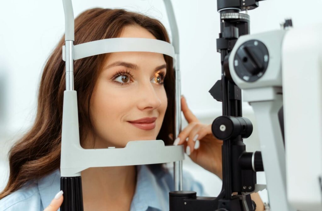 A smiling patient resting her chin and forehead on a slit lamp during a comprehensive eye examination.
